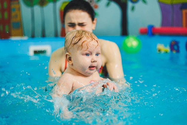 A female trainer teaches a baby to swim in the pool and supports his hands Baby swimming in the pool Teaching a newborn boy to swim in the pool