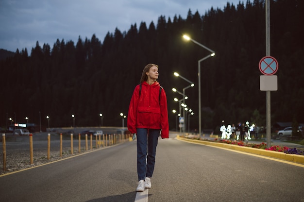 Female traveler in a red raincoat strolling near the mountain coniferous forest