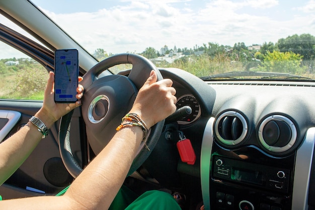 Female traveler sits behind the wheel and checks the route on the map on the smartphone screen