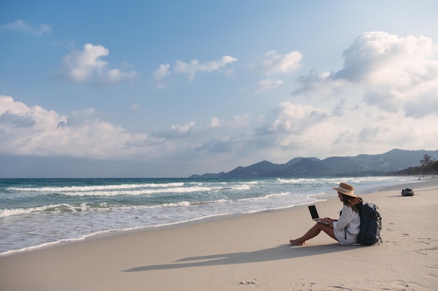 A female traveler using and working on laptop computer while sitting on the beach