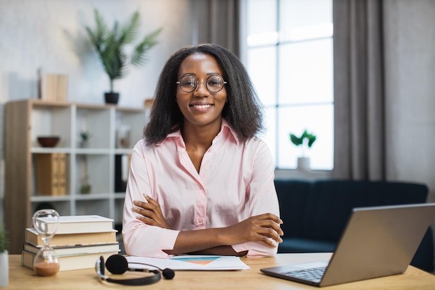 Female tutor in eyeglasses sitting at desk with books