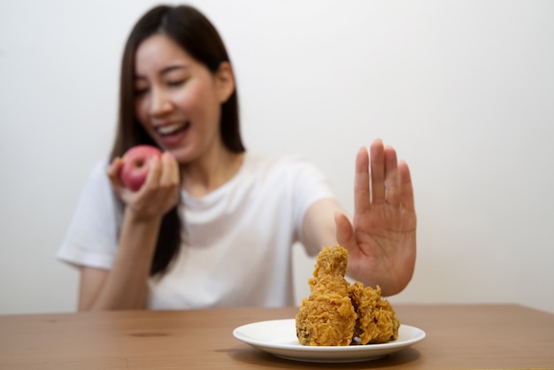 female using hand reject junk food by pushing out her favorite fried chicken and choose red apple and salad for good health.