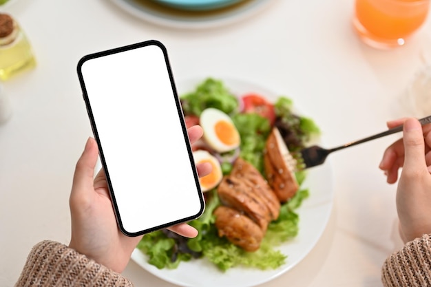 Female using smartphone while eating healthy organic grilled chicken salad