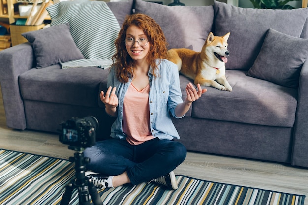 Female vlogger recording video at home with cute dog sitting on floor using camera