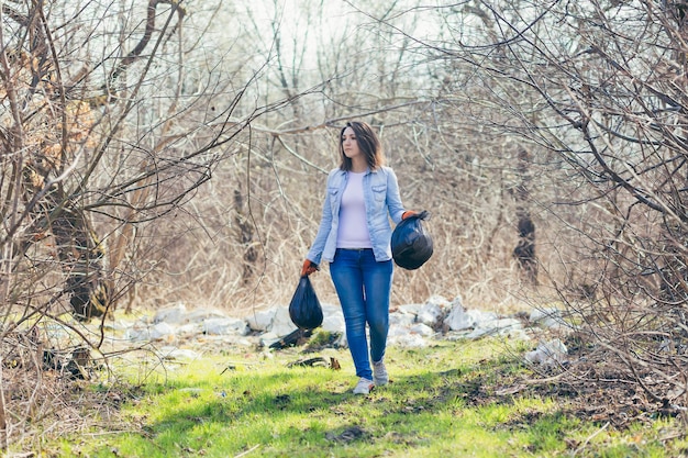 Female volunteer holds bags with collected plastic cleaning the forest and park from garbage