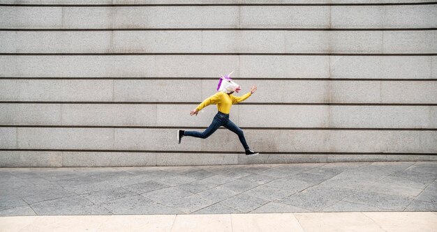 Female wearing vibrant unicorn mask jumping against wall