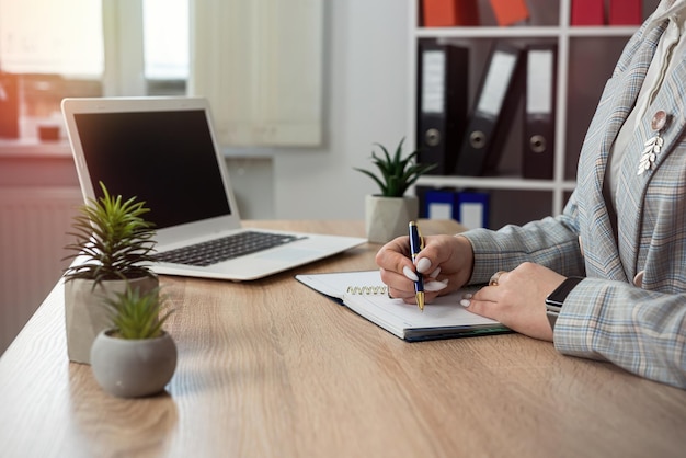 female web designer making notes in notepad use lapton on office workplace