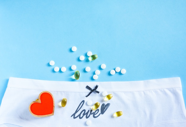 Female white panties with grew bow and word love, heart and pills on blue