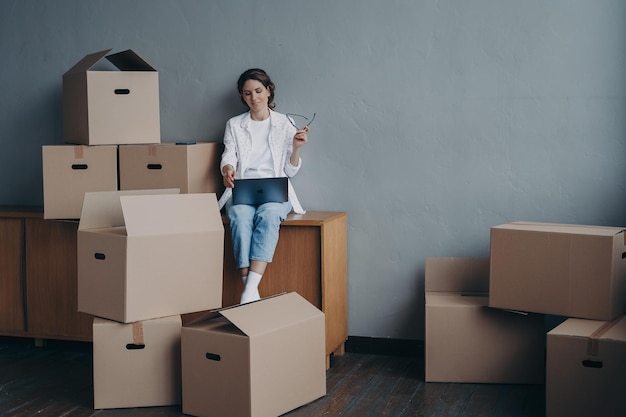 Female with carton boxes searching moving company at laptop for relocation Transportation service