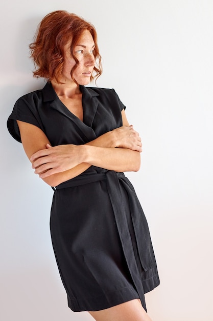 female with freckles and natural red hair posing at camera and looking away, wearing black dress