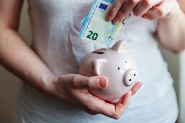 Female woman hands holding pink piggy bank and putting money Euro Saving investment budget business wealth retirement financial money banking concept