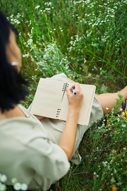 Female woman with pen writing or painting handwriting on notebook on flower blooming meadow