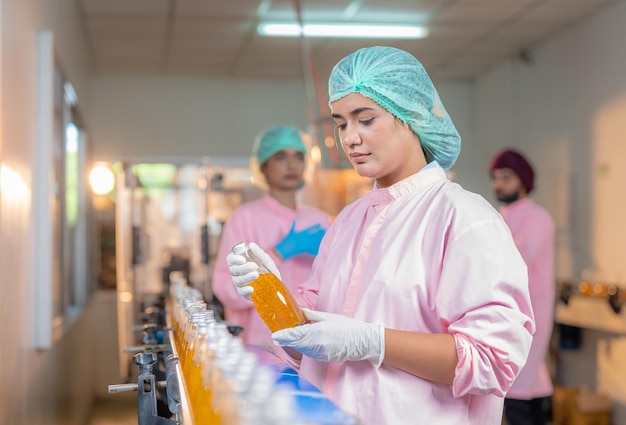 Female worker checking quality of fruit juice drink bottle in production line beverage factory