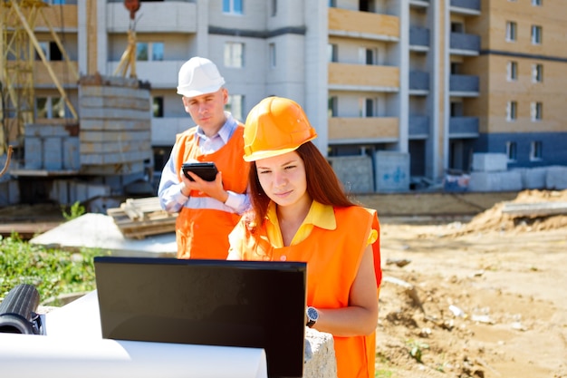 Female worker and construction worker looking at laptop together against construction