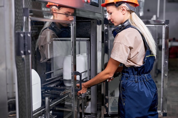 Female worker in factory preparing robotic line for bottling and packing canisters.