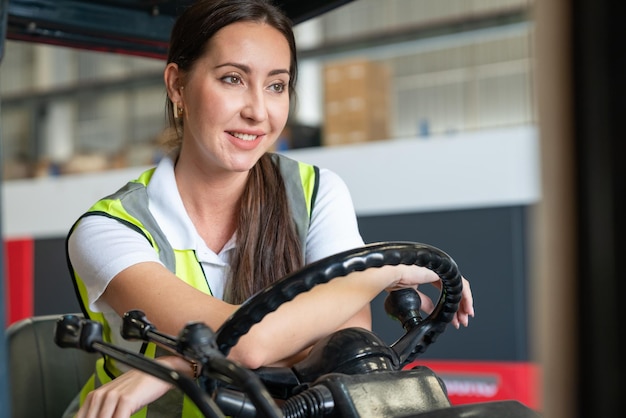 Female worker in safety vest driver operating forklift in logistic shipping warehouse factory