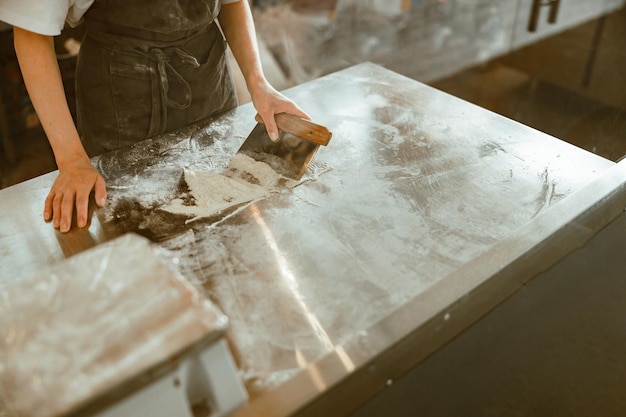 Female worker stands at table with pile of white flour and cutting tool in bakery