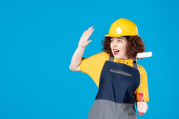 Female worker in uniform with paintroller on blue