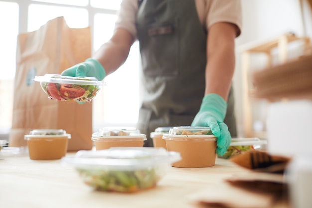 female worker wearing protective gloves while packaging orders at food delivery service