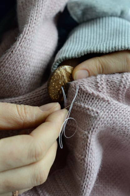 Female workers' hands sew a wooden button to a jacket. close-up.