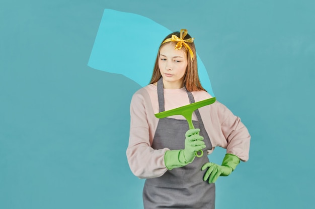 Female young janitor using a squeegee to clean a window wearing an apron and gloves as he works