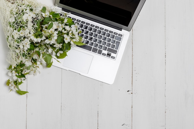 Feminine business concept with laptop, spring flowers bouquet and woman's hands holding cup of warm tea or coffee