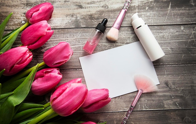 Feminine desk workspace with cosmetics lipstick and tulip flowers on wooden background