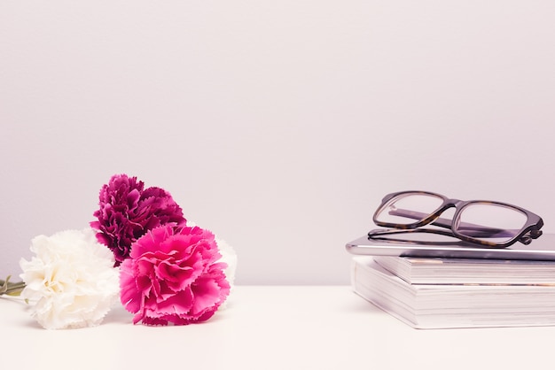 Feminine desktop bedside table with book, glasses, flowers and negative space.