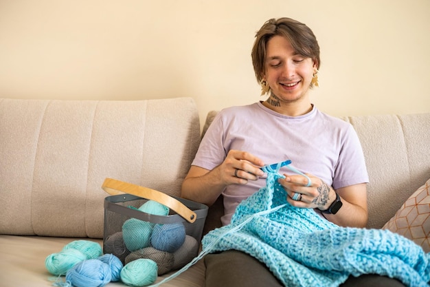 Photo feminine hipster man crochet handmade use hook knitting needles and wool yarn relaxing on couch