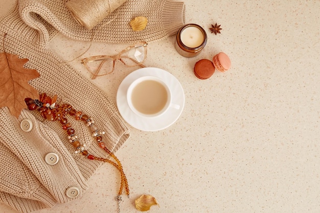 Feminine trendy outfit sweater glasess and brown gemstone jewellery Autumn aesthetic coffee time among candle fall leaves macaroons Pastel background