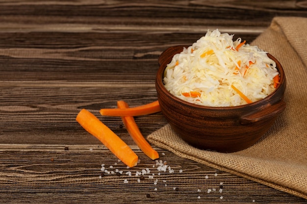 Fermented cabbage Sauerkraut with carrots in clay bowl on wooden background  Vegan food