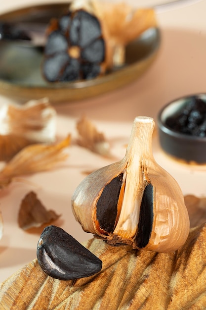 Fermented garlic head and garlic clove on a handmade wooden plate A small clay bowl with black garlic paste in the background Healthy and fermented food photo composition selective focus