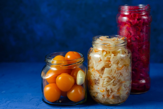 Fermented pickled vegetables in various modern glass jars, ready for closing. white and red with beetroot cabbage and yellow cherry tomatoes with garlic on a classic blue wall