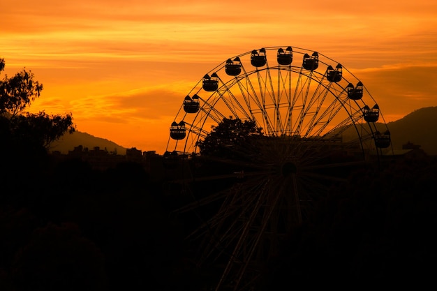 A ferris wheel is silhouetted against a sunset sky.