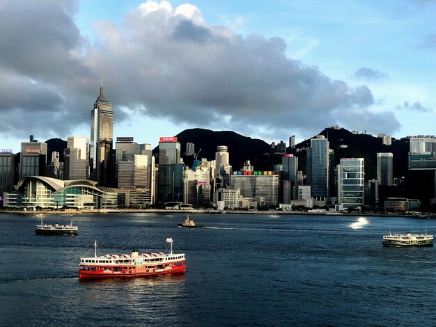 Photo ferry in victoria harbour by buildings against sky in hong kong