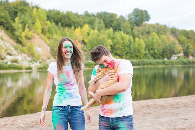 Festival holi, holidays, tourism, pet and nature concept - Portrait of woman and man with cat covered multi-colored dust.