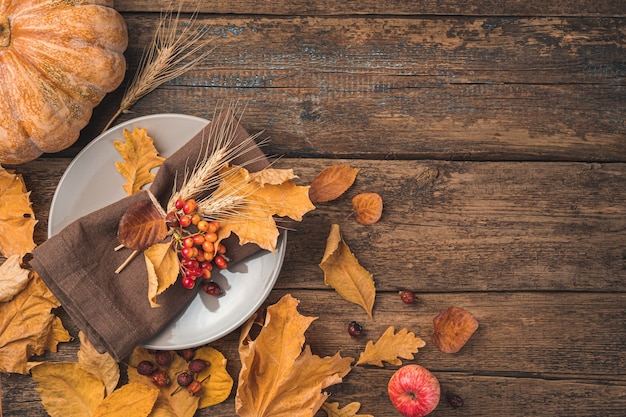 Festive autumn background with a plate cutlery napkin pumpkin and autumn leaves on a wooden background