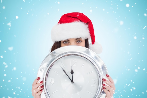 Festive brunette holding a clock against blue vignette