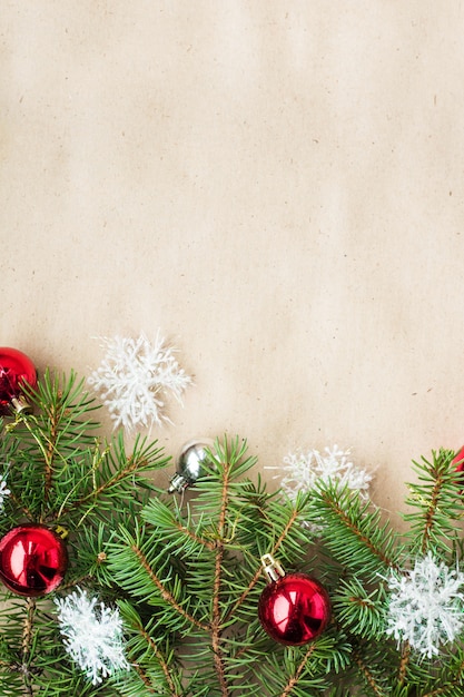 Festive christmas border with red and silver balls on fir branches and snowflakes on rustic beige surface