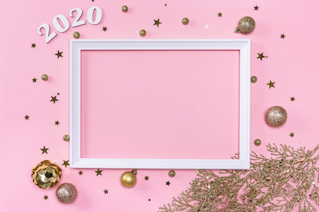 Festive christmas frame made of golden balls, fir tree branches, decorations and confetti on pastel pink background.