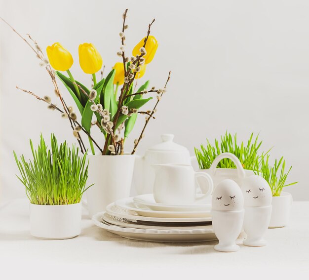 Festive composition Easter eggs in glasses white dishes and willow tulips on a white table Happy Easter concept