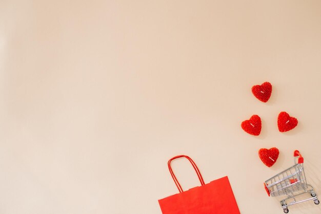 Festive composition gift paper red bag hearts with a shopping basket on a beige background with a place to copy the text Shopping online for Valentines Day Flat lay top view