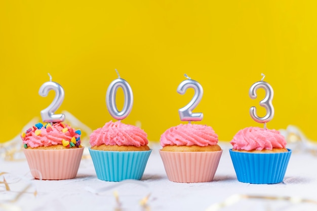 Festive cupcakes and candles in form of numbers 2023 on yellow background Concept of New year