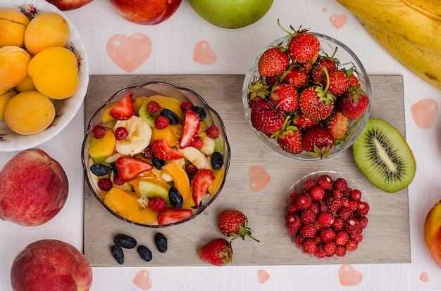 Festive dessert fruit salad with strawberries and strawberries and fruits with hearts on a white surface. Valentine's Day. Birthday. Raw food diet