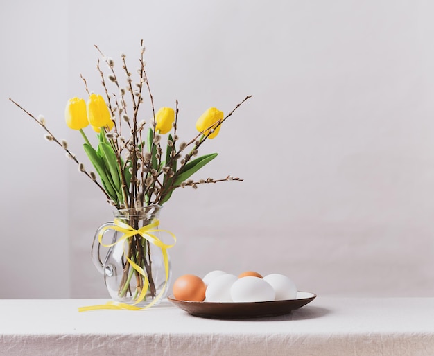 Festive Easter eggs in a clay plate a vase with yellow tulips and willow branches on the table Happy Easter concept