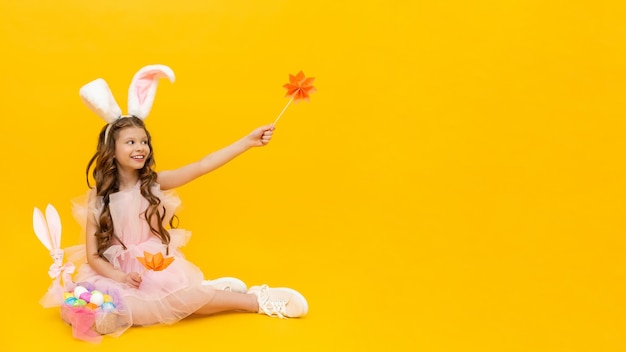 Festive Easter A happy little girl is sitting and enjoying the spring holiday A child with rabbit ears on a yellow isolated background Copy space