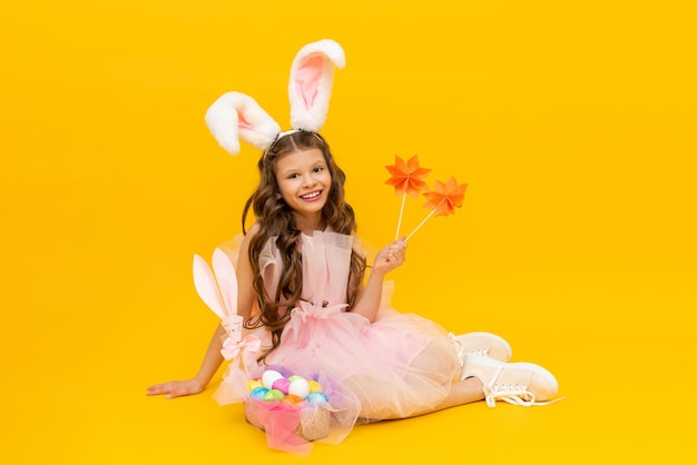 Festive Easter A happy little girl is sitting and enjoying the spring holiday A child with rabbit ears on a yellow isolated background