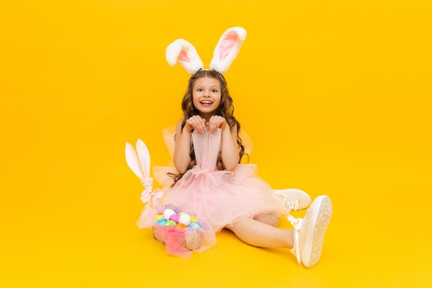 Festive Easter A little girl depicts an Easter bunny with a basket of colorful eggs A child with rabbit ears on a yellow isolated background