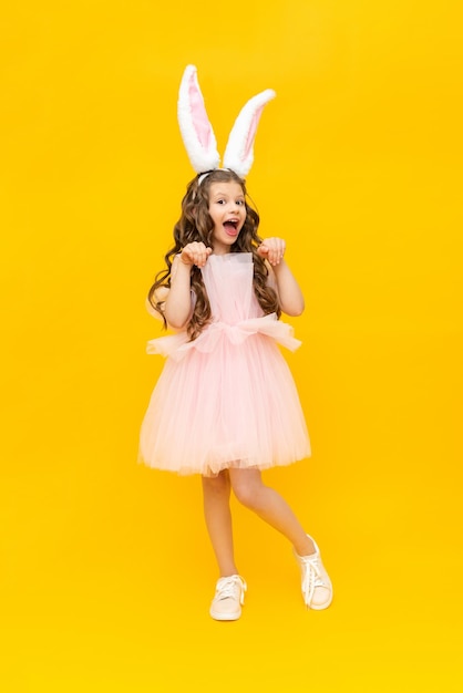 Festive Easter A teenage girl in a fluffy dress and with rabbit ears is smiling broadly A beautiful little girl in a rabbit costume on a yellow isolated background fulllength