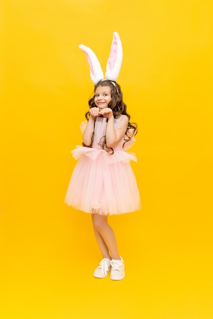 Festive Easter A teenage girl in a fluffy dress and with rabbit ears is smiling broadly A beautiful little girl in a rabbit costume on a yellow isolated background fulllength